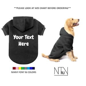 Op de afbeelding: Zwarte hoodie voor honden met de tekst "Your Text Here" in wit. De hoodie wordt getoond op een golden retriever. De afbeelding toont ook een kleurenkaart met veel lettertype- en kleuropties.