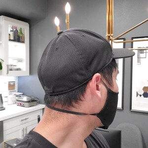 May include: A black mesh baseball cap with a black face mask. The cap has a curved brim and a black strap.
