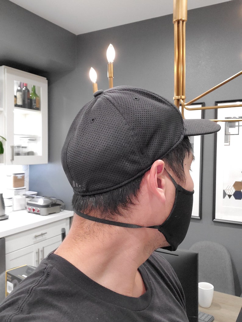 May include: A black mesh baseball cap with a black face mask. The cap has a curved brim and a black strap.