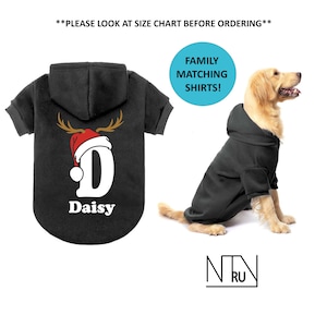 May include: Black hooded dog sweatshirt with a reindeer antler and Santa hat design, the letter "D", and the name "Daisy". A dog wears a matching black hoodie. Text: "Family Matching Shirts!"