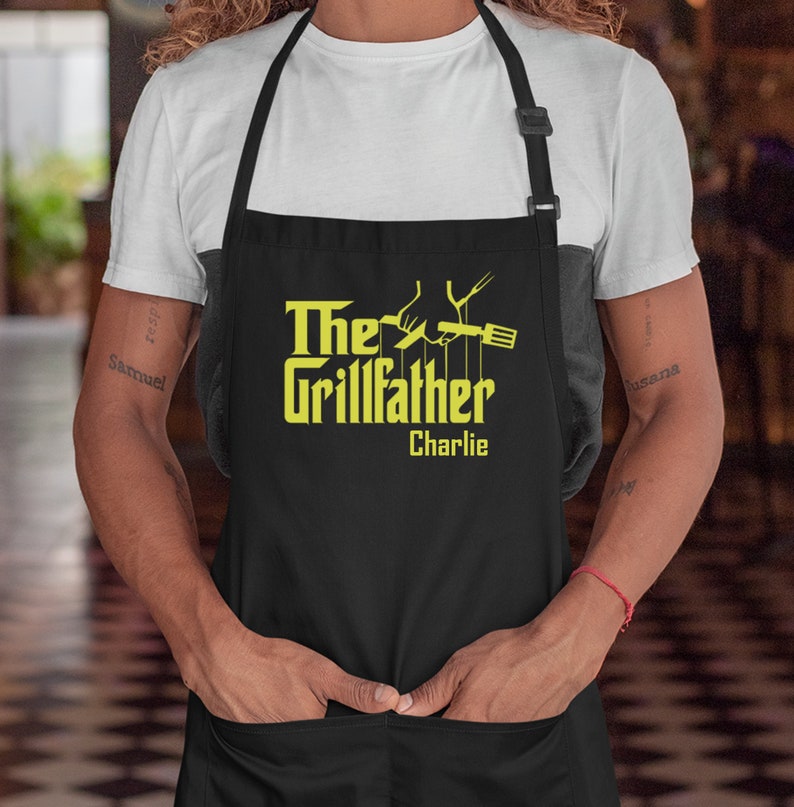 May include: Black apron with a yellow graphic that says "The Grillfather" with a hand holding a spatula and a fork. The name "Charlie" is written below the graphic.