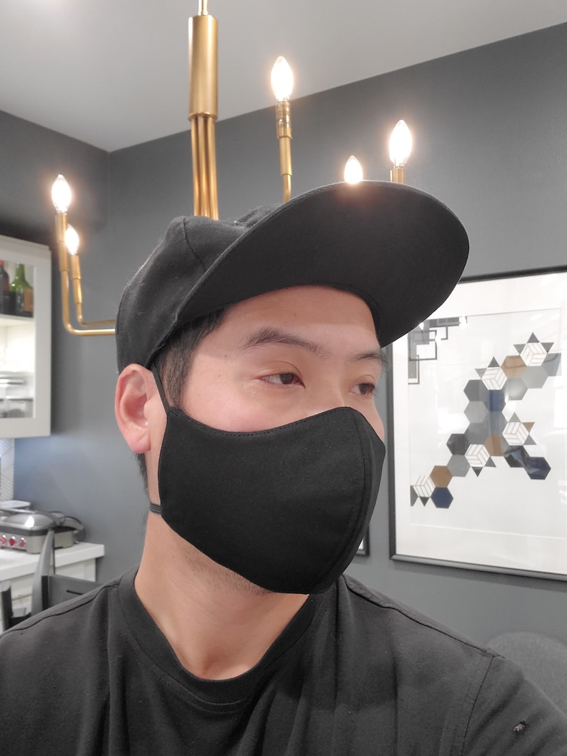 May include: A person wearing a black face mask and a black baseball cap. The mask is made of a soft, breathable fabric and has a comfortable fit.