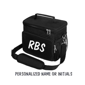 Puede incluir: Bolsa de almuerzo aislada negra con una correa para el hombro y un asa superior. La bolsa tiene un cierre de cremallera y un bolsillo lateral de malla. Las iniciales "RBS" est&aacute;n impresas en blanco en la parte delantera de la bolsa.