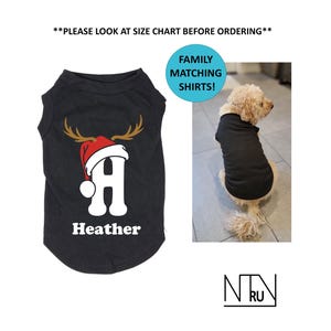 May include: Black dog shirt with a reindeer antler and Santa hat design, featuring the letter "A" and the name "Heather". The image also includes a dog wearing a black shirt and the text "FAMILY MATCHING SHIRTS!"