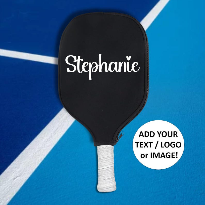 May include: A black pickleball paddle with a white handle and the name "Stephanie" written on the face. The paddle is on a blue and white surface. Add your text, logo, or image!