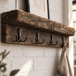 Puede incluir: Un perchero de pared fabricado con una pieza gruesa de madera oscura recuperada con una superficie rugosa y texturizada. Cuenta con cuatro ganchos dobles de metal oscuro fijados en la parte frontal y un estante superior plano para objetos.