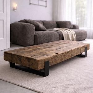 Peut inclure: Table basse rectangulaire en bois de récupération avec une finition naturelle. Elle repose sur des pieds en métal noir. La table est dans un salon avec un canapé gris et un tapis de couleur neutre. Mesure environ 180 cm de long.