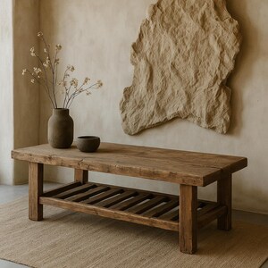 May include: A rustic, rectangular wooden coffee table with a lower shelf. The table is made of reclaimed wood with visible grain and knots. A vase with dried flowers and a small bowl sit on top. The table is 60 inches long, 20 inches wide, and 18 inches high.