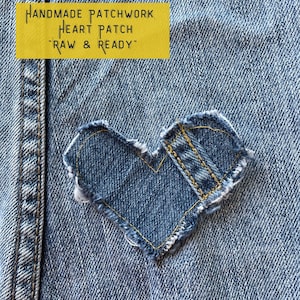 May include: A denim heart patch sewn onto a blue denim fabric. The patch is made of denim scraps and has a raw edge. The text "HANDMADE PATCHWORK HEART PATCH 'RAW & READY'" is printed on a yellow background.