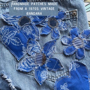 May include: Handmade flower patches made from a vintage 1970s bandana. The patches are blue with white floral patterns and are sewn onto a denim background. The text "HANDMADE PATCHES MADE FROM A 1970S VINTAGE BANDANA" is visible.