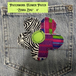 May include: A denim pocket with a colorful patchwork flower applique. The flower features zebra print, pink, green, and patterned fabrics. The text on the label reads "PATCHWORK FLOWER PATCH" and "Zebra Zing" 4".