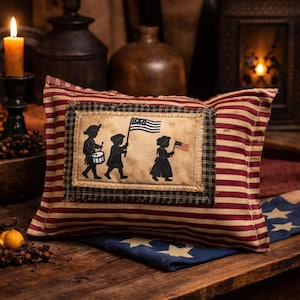Op de afbeelding: Rechthoekig decoratief kussen met een patriottisch thema. Het kussen heeft een centrale patch met silhouetten van kinderen die vlaggen en een trommel dragen. Het kussen heeft rood-cr&egrave;mekleurige strepen en een zwart-cr&egrave;mekleurige geruite rand.