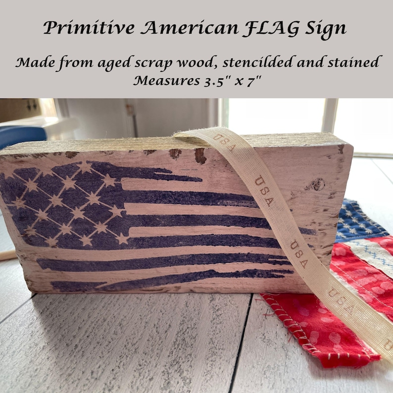 May include: A rustic wooden sign featuring the American flag design, stenciled in blue and white. The sign is made from aged scrap wood and measures 3.5 inches by 7 inches. A ribbon with "USA" text is draped across the sign.