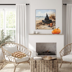 May include: A black witch's hat with a wide brim sits on a sandy beach with three orange pumpkins. The hat is decorated with a brown band and a black buckle. The beach is surrounded by tall grass and a blue sky with white clouds.