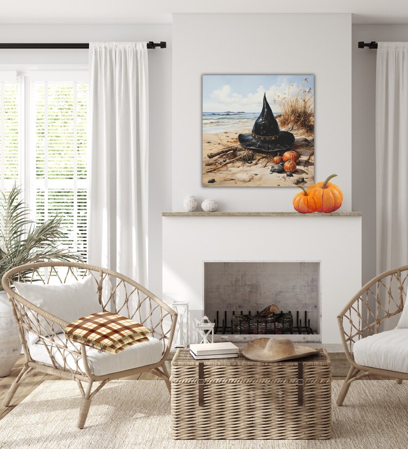 May include: A black witch's hat with a wide brim sits on a sandy beach with three orange pumpkins. The hat is decorated with a brown band and a black buckle. The beach is surrounded by tall grass and a blue sky with white clouds.