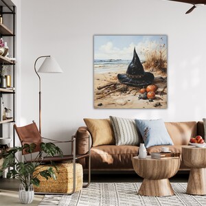 May include: A black witch's hat sits on a sandy beach with three small orange pumpkins. The hat is made of a dark fabric and has a wide brim. The pumpkins are arranged in a small pile in front of the hat.