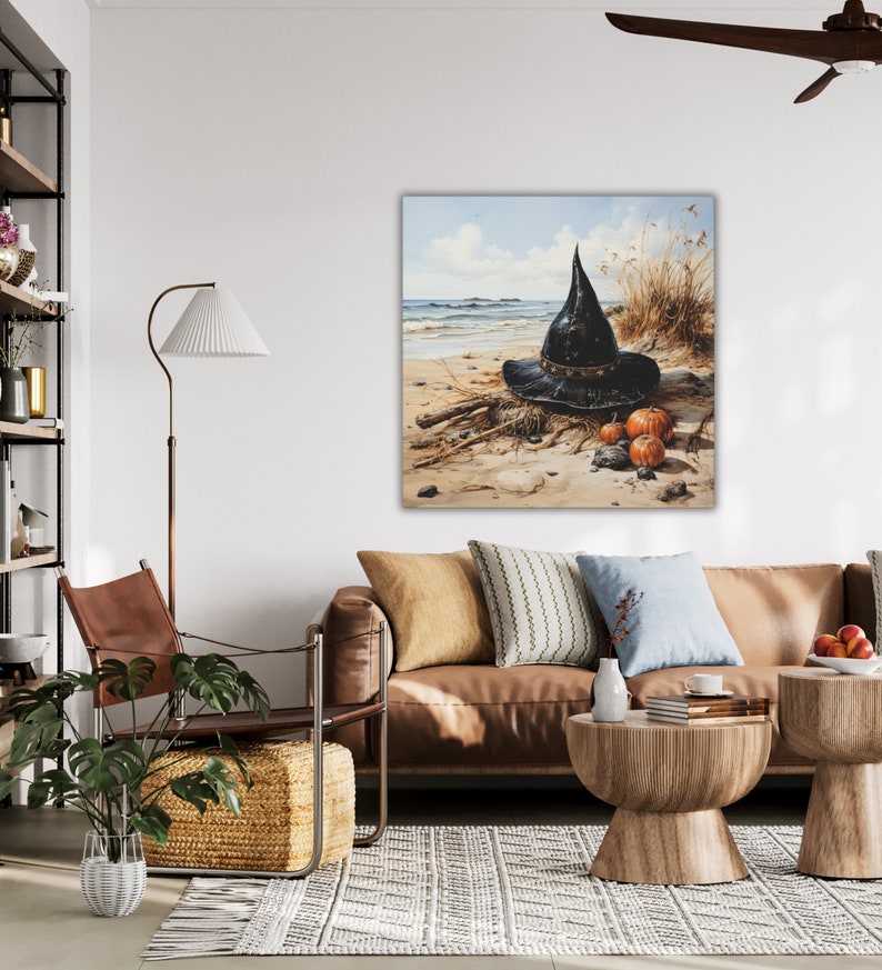May include: A black witch's hat sits on a sandy beach with three small orange pumpkins. The hat is made of a dark fabric and has a wide brim. The pumpkins are arranged in a small pile in front of the hat.