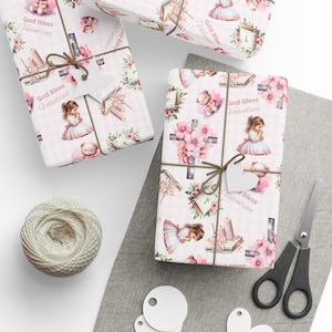 May include: Pink and white wrapping paper with a repeating pattern of a girl praying, a teddy bear, a book, a cross, and flowers. The text "God Bless Valentina" is repeated throughout the pattern.