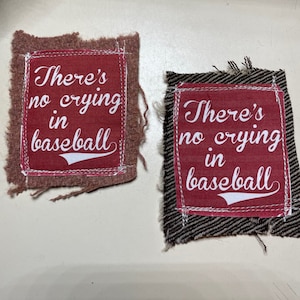 May include: Two red fabric patches with frayed edges. The patches have white text that reads "There's no crying in baseball" and a white baseball graphic.