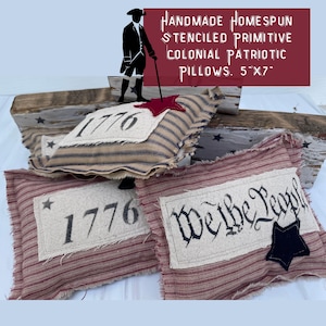 May include: Three handmade, primitive, patriotic pillows with red, white, and blue striped fabric. One pillow features the year "1776" in black lettering, another pillow features the phrase "We the People" in black lettering, and the third pillow features a red star and the year "1776" in black lettering. The pillows are 5 inches by 7 inches.