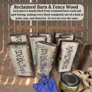 May include: Reclaimed barn wood blocks with the text "We the People" in black script. The blocks are rectangular, with a distressed white paint finish. A can of wood stain and a blue glove are in the foreground.