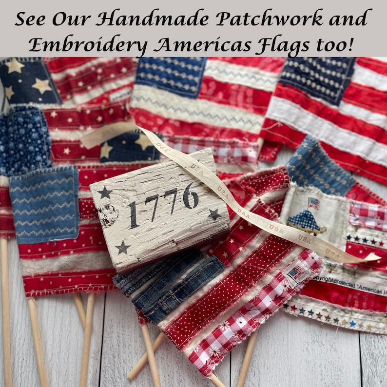 May include: Handmade patchwork and embroidered American flags in red, white, and blue. The flags feature stars and stripes, with some flags mounted on wooden dowels. A wooden block with "1776" is also present.