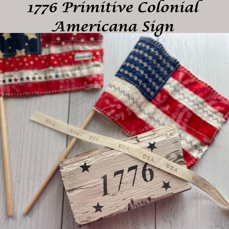 May include: A rustic wooden sign with the number "1776" and star accents, accompanied by two miniature American flags. A ribbon with "USA" text is draped across the sign. The flags feature red and white stripes and blue fields with white stars.