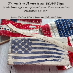 May include: Aged wood sign with a stenciled American flag design. The sign measures 3.5" x 7" and is stenciled in black iron or colonial blue. The image also shows a ribbon with "USA" printed on it and a fabric American flag.