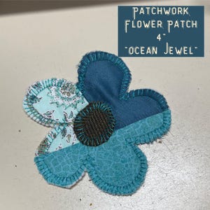 May include: A 4-inch patchwork flower patch titled Ocean Jewel, featuring teal, light blue, and patterned fabric petals with dark blue stitching and a textured brown center. The design includes a dark blue petal, a light blue floral petal, and a textured teal petal.