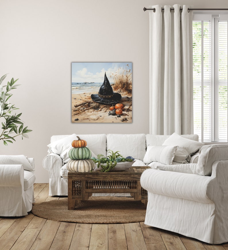 May include: A black witch's hat sits on a sandy beach with three small pumpkins. The hat has a pointed top and a wide brim. The pumpkins are orange and green. The background is a blue sky with white clouds.