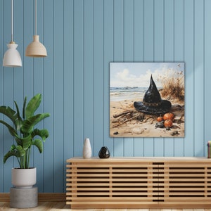 May include: A black witch's hat with a wide brim sits on a sandy beach with three small pumpkins. The hat is made of felt and has a pointed crown. The pumpkins are orange and have a stem on top. The background is a blue sky with white clouds.