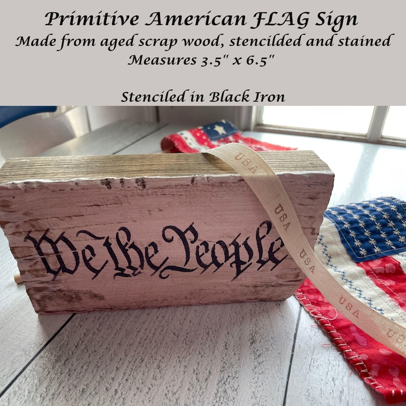 May include: A rustic, rectangular sign made from aged wood, stenciled with "We the People" in black iron. The sign measures 3.5" x 6.5" and features a distressed, whitewashed finish. A ribbon with "USA" text is draped across the sign.