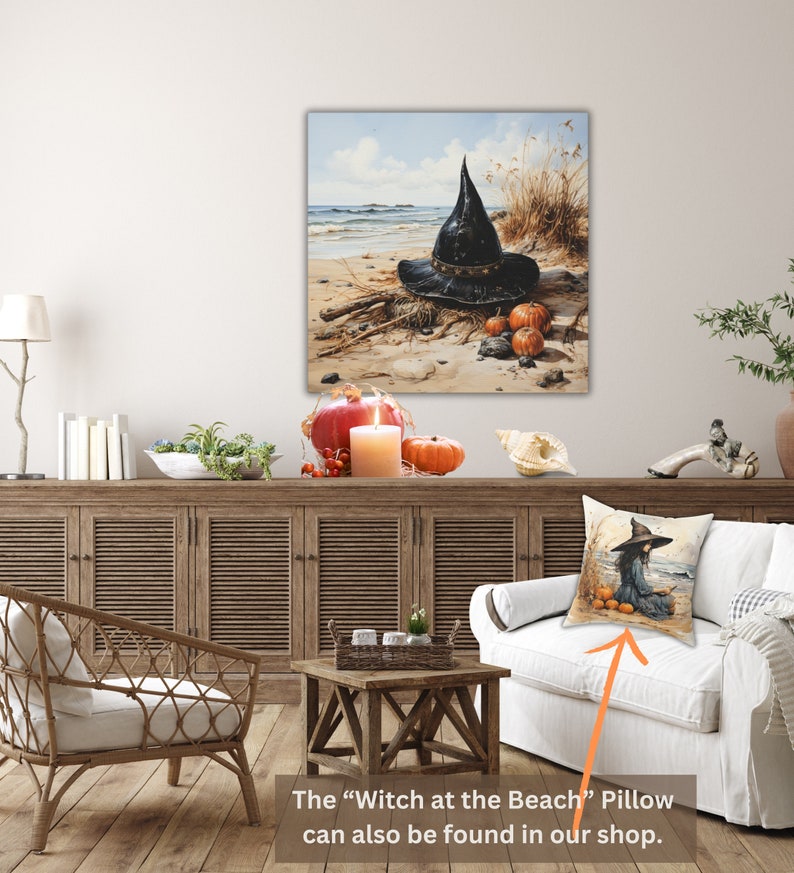 May include: A black witch's hat with a wide brim sits on a sandy beach with pumpkins and driftwood. The hat is decorated with a black band and a buckle. The beach is surrounded by tall grasses and a blue sky with white clouds.