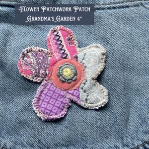 May include: A flower-shaped patchwork patch featuring various fabric patterns in pink, purple, and grey, with a central circular accent. The text 'FLOWER PATCHWORK PATCH GRANDMA'S GARDEN 4"' is visible above the patch, which is attached to blue denim.