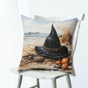 May include: A black witch's hat with a star-shaped band sits on a sandy beach with dried seaweed and three small orange pumpkins.