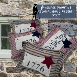 May include: Four handmade primitive colonial bowl fillers, each measuring 5 inches by 7 inches. The fillers are made of fabric with red, white, and blue stripes and feature the numbers "1776" and the text "We the People".