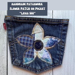 May include: A denim pocket with a handmade patchwork flower design. The flower features blue plaid, floral, and striped fabric pieces, stitched with gold thread. Text on top reads "HANDMADE PATCHWORK FLOWER PATCH ON POCKET" and "LEVIS 501".