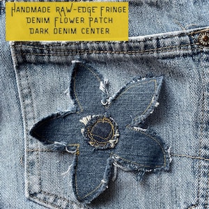 May include: A denim flower patch with raw-edge fringe. The flower is made from dark denim and has a light denim center. The text "HANDMADE RAW-EDGE FRINGE DENIM FLOWER PATCH DARK DENIM CENTER" is printed on a yellow background.