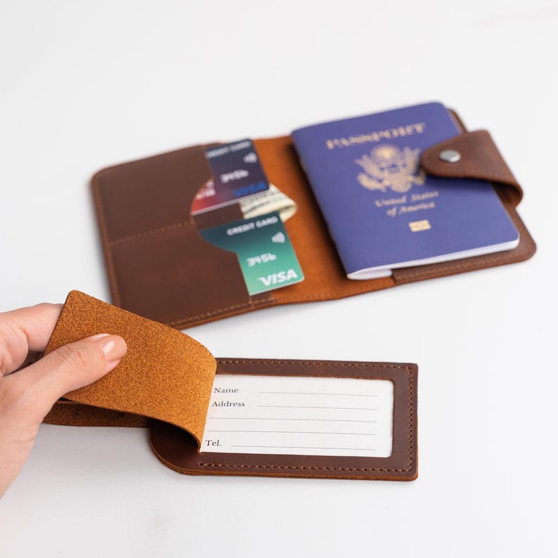 May include: A brown leather passport holder with a separate luggage tag. The passport holder has multiple slots for credit cards and cash. The luggage tag has a clear window for a name, address, and phone number.