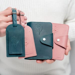 May include: Two teal leather passport holders and two teal leather luggage tags with the names "Stephanie" and "Jessica" embossed on them. Each holder and tag features a floral design.