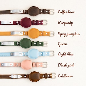 Op de afbeelding: Een collectie leren hondenhalsbanden in diverse kleuren, waaronder koffieboon, bordeauxrood, spicy pumpkin, groen, lichtblauw, blush roze en coldbrew. Elke halsband heeft een metalen naamplaatje en een cirkelvormig leren detail.