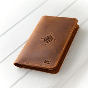 May include: A brown leather passport holder with a compass design and the initials "MD" embossed on the front.
