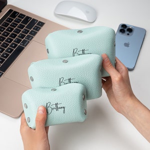 May include: Three light blue leather pouches with the name "Brittany" printed in black on each. The pouches are stacked on top of each other.