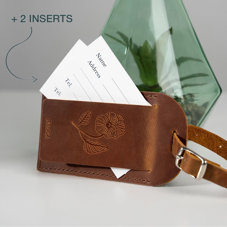 May include: Brown leather luggage tag with a floral design and the name "JESSICA" embossed on the front. The tag has a slot for a white card insert with fields for name, address, and phone number. The text " + 2 INSERTS" is visible in the top left corner of the image.