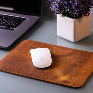 May include: A brown leather desk mat with the text "BOSS LADY" printed on it. A white wireless mouse is on the mat.