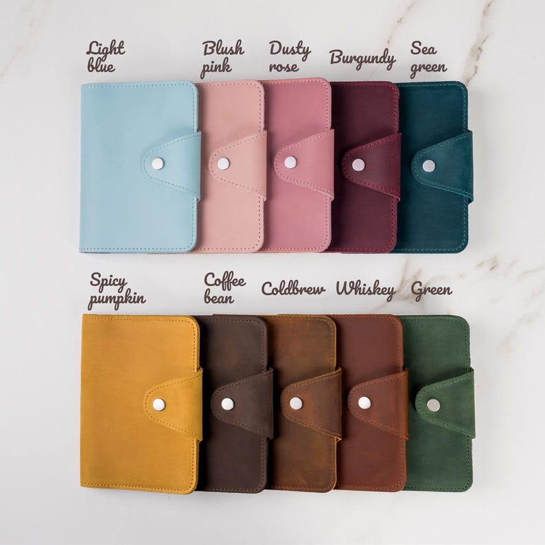 May include: A set of ten leather wallets in various colors, including light blue, blush pink, dusty rose, burgundy, sea green, spicy pumpkin, coffee bean, cold brew, whiskey, and green. Each wallet has a flap with a button closure.