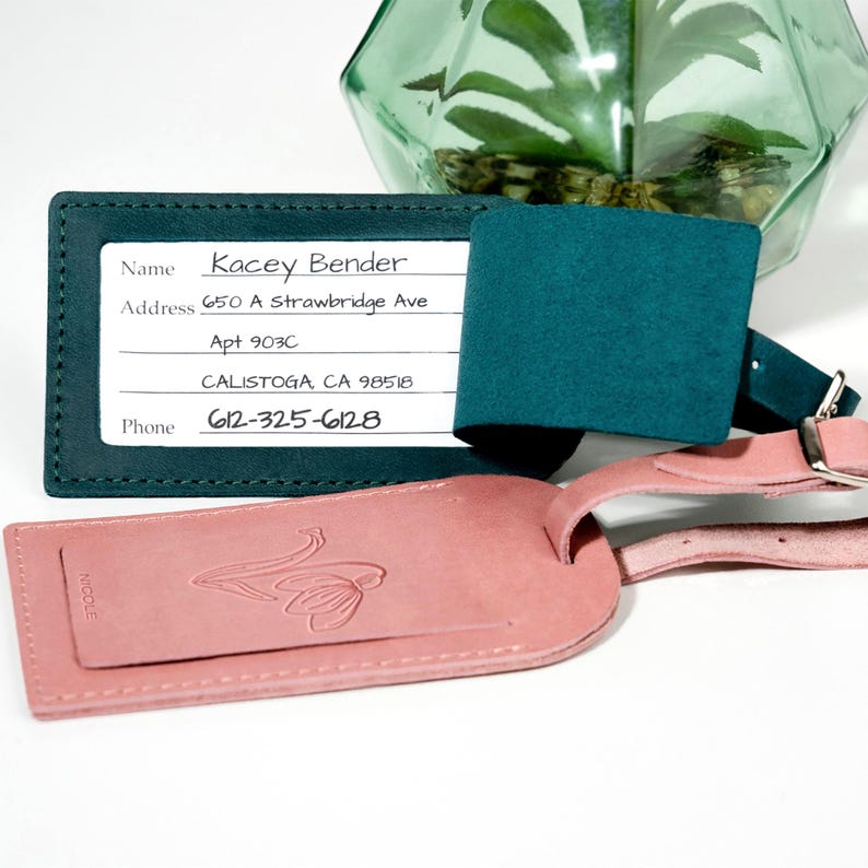 May include: A teal leather luggage tag with a white label that says "Kacey Bender" and includes an address and phone number. The tag is attached to a pink leather luggage tag with a floral design.