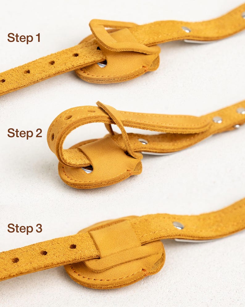 Op de afbeelding: Close-up van een mosterdgele leren riem met een gesp, die de bevestigingsstappen laat zien. De teksten "Stap 1", "Stap 2" en "Stap 3" zijn zichtbaar. De riem heeft gaten en zilveren klinknagels.