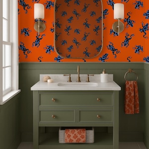 May include: A bathroom with orange walls patterned with blue frog illustrations. The vanity is olive green with a white countertop and gold fixtures. A matching rug and towel complete the design.