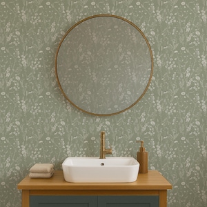 May include: A bathroom scene featuring a round gold-framed mirror, a white rectangular sink, and a wooden vanity with a green cabinet. The wall is covered in a green floral wallpaper. A gold faucet and soap dispenser are visible.